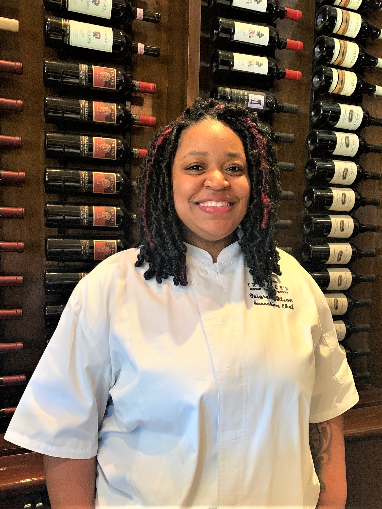 picture of Chef Paigton in front of the wine wall at the restaurant