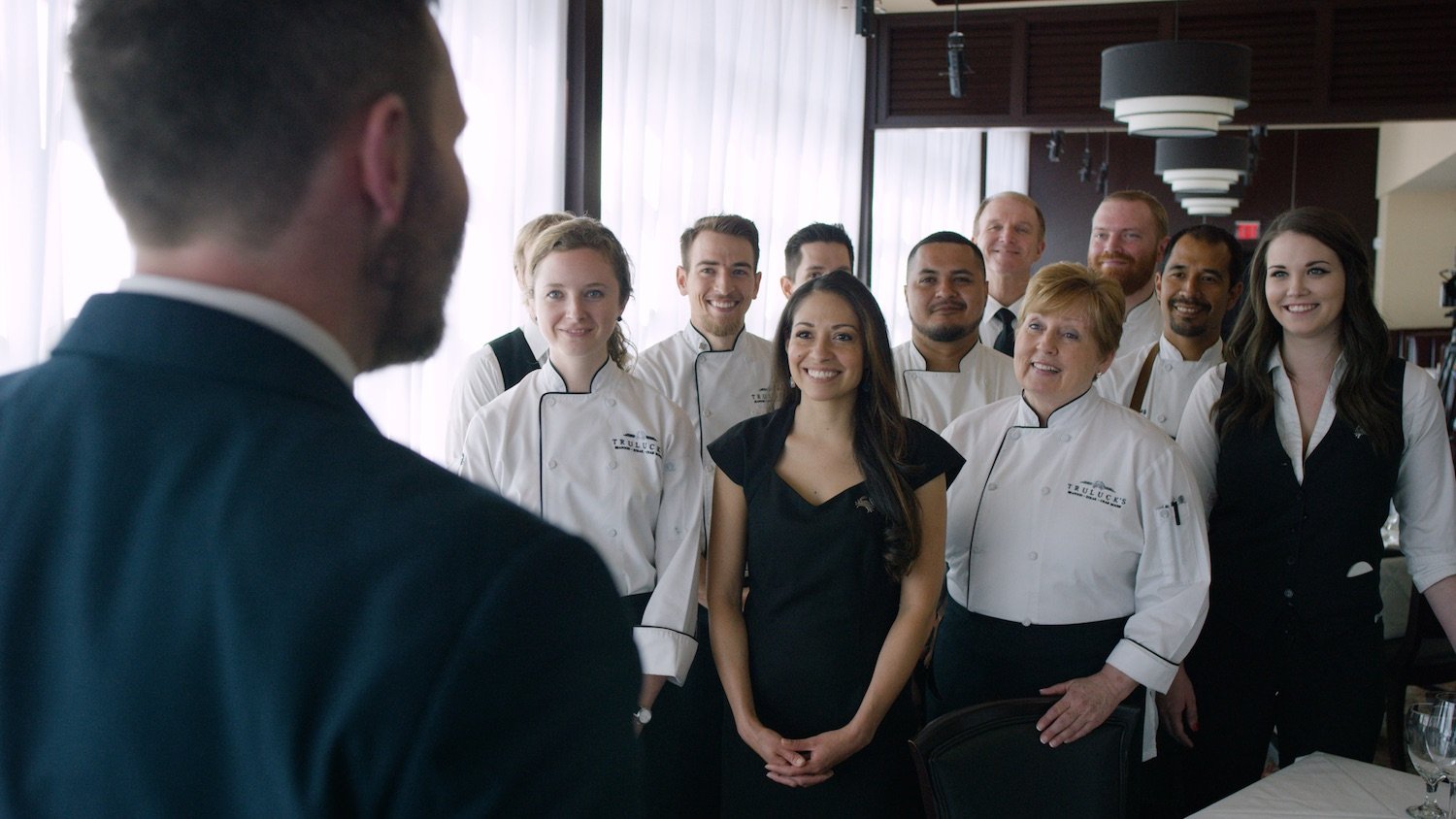 picture of Team of Truluck's staff and chefs smile while listening to head manager