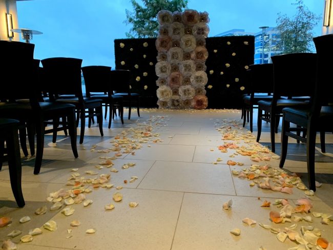 picture of Truluck's Woodlands wedding event with a floor to ceiling paper flower installed background for the couple to marry in front of. Chairs are setup in rows for the ceremony overlooking the water.