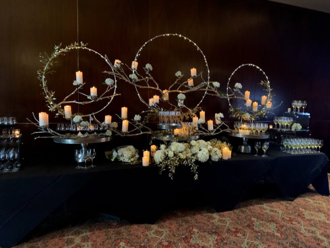 picture of Truluck's Woodlands private event with a magical wine display to include 3 large silver rings with lots of white pillar candles. The table is setup as a wine tasting station with various red, white and sparkling varietals