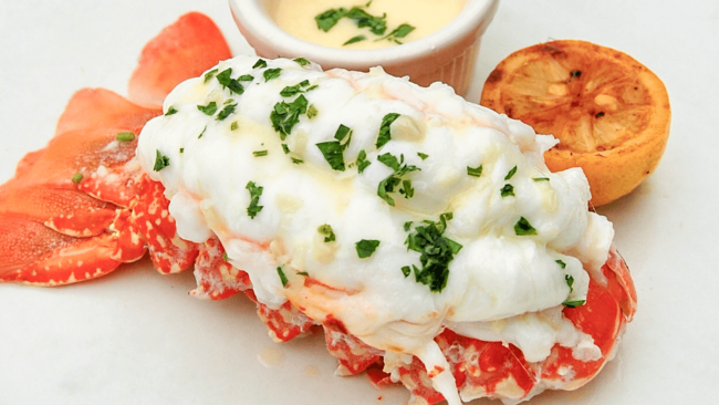 picture of a Truluck's South African lobster tail topped with parsley and with butter dipping sauce and a charred half lemon