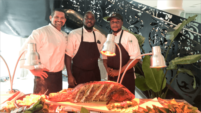 picture of Chef Odel with his fellow chefs preparing to serve a giant grouper fish